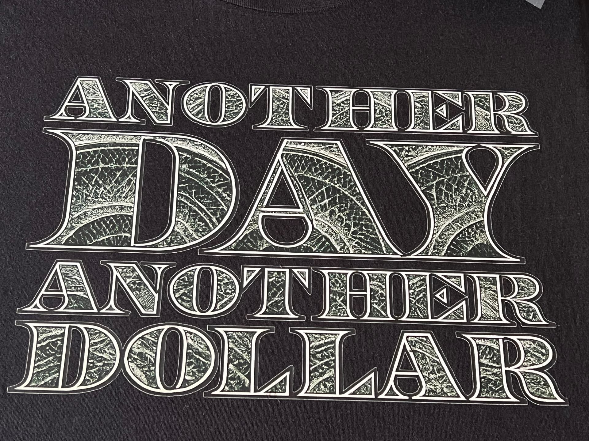 Black t-shirt with an ornate silver-style print that reads Another Day Another Dollar