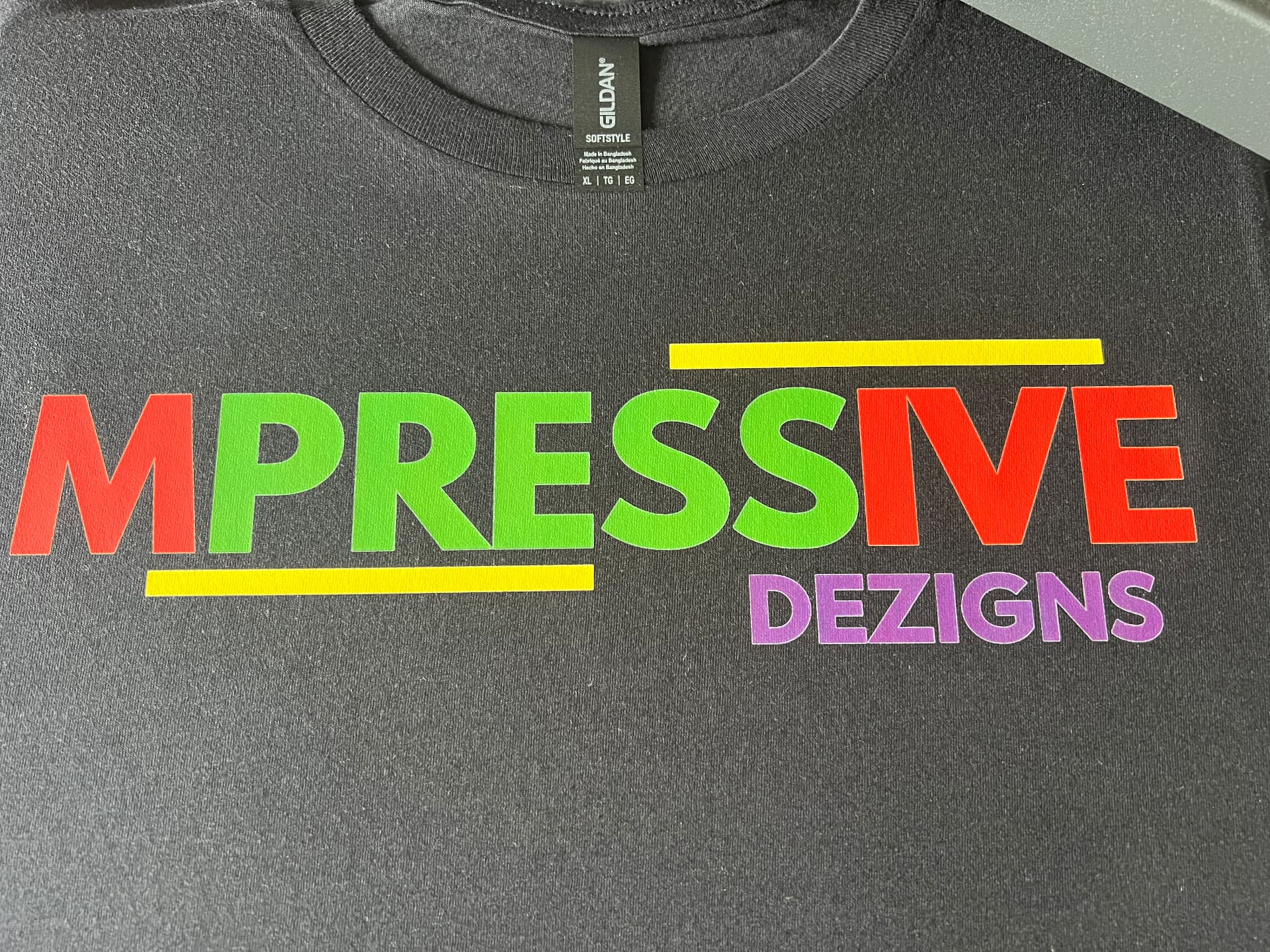 Black t-shirt printed with the Mpressive Dezigns logo in red, green, yellow and purple